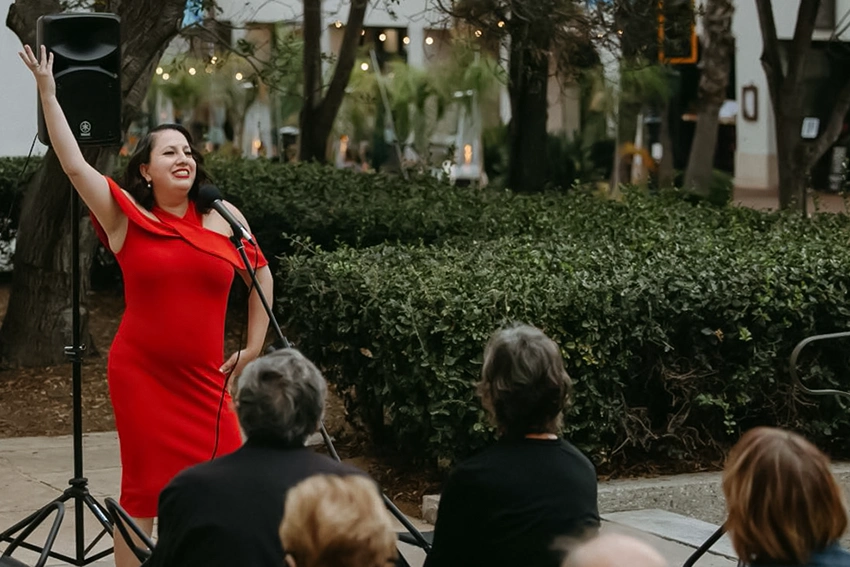 singer in a red dress posing with her arm raised in front of a crowd on terrace